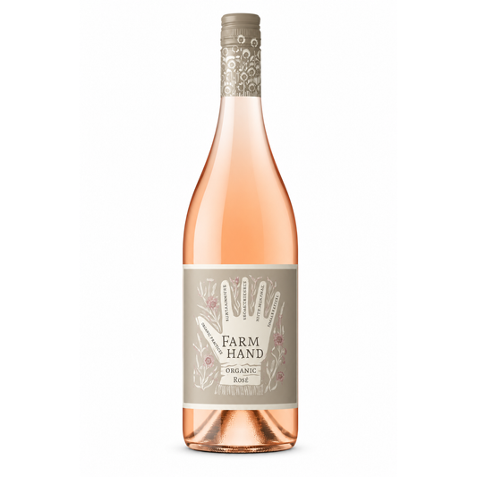 A bottle of Farm Hand Organic Rose wine with a pale pink liquid, a beige label featuring a hand illustration, and a silver-gray cap, shown on a plain white background.